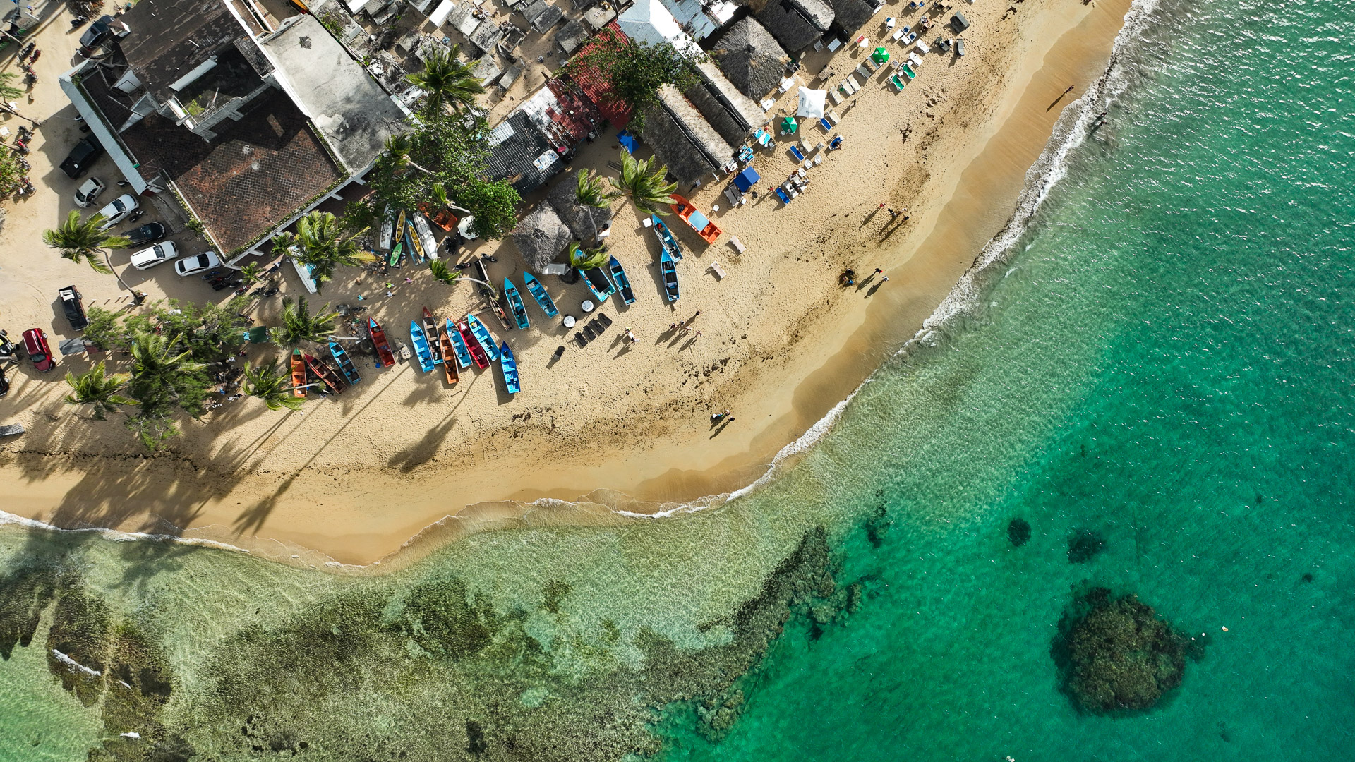 Pogled z dronom na peščeno plažo Las Terrenas v Dominikanski republiki, pisane ribiške čolne, palme in turkizno Karibsko morje.